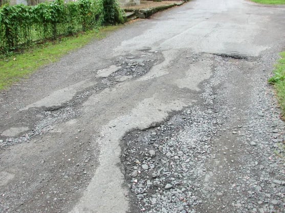 Picture show bad roads with potholes and uneven surface.