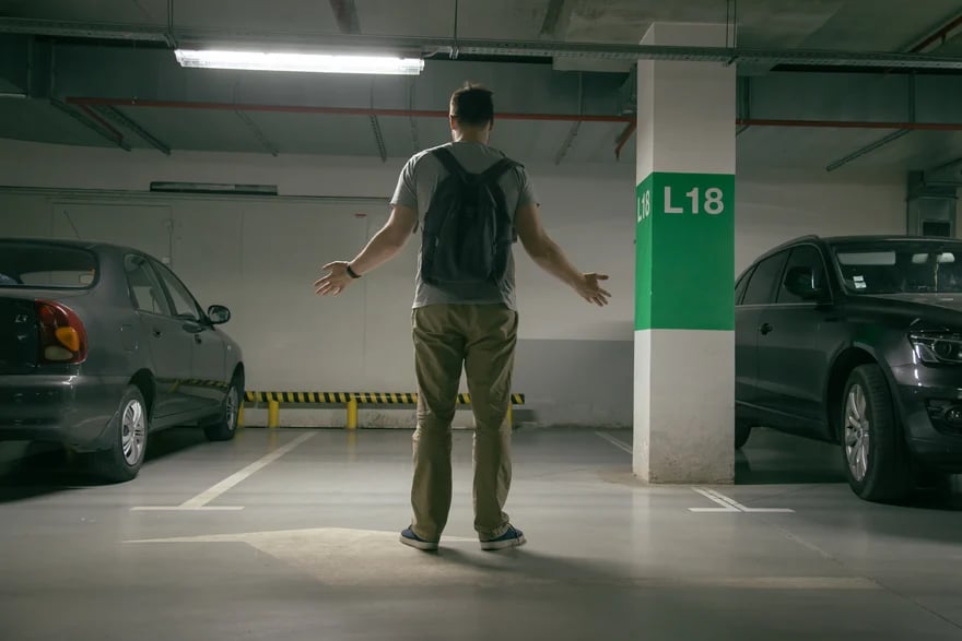 Man with a backpack standing in front of an empty parking spot in a garage looking for his Missing Car 