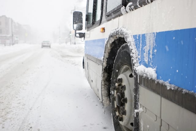 transit bus travelling through a snowy city street in the winter time.