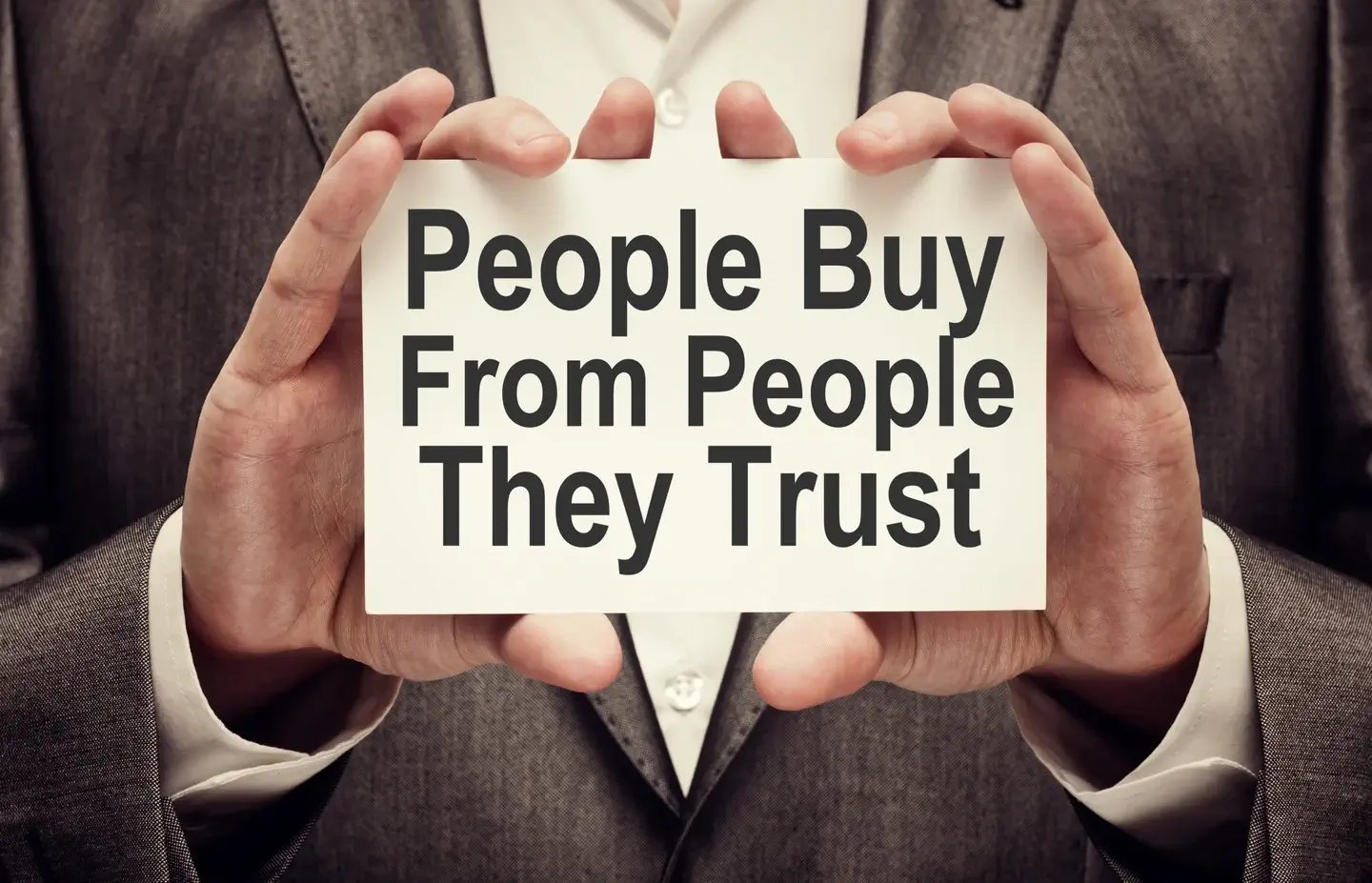 Man holding a piece of paper with the statement, People Buy From People They Trust-