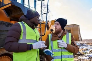 two-workers-next-to-idling-construction-vehicle-chatting-and-having-coffee