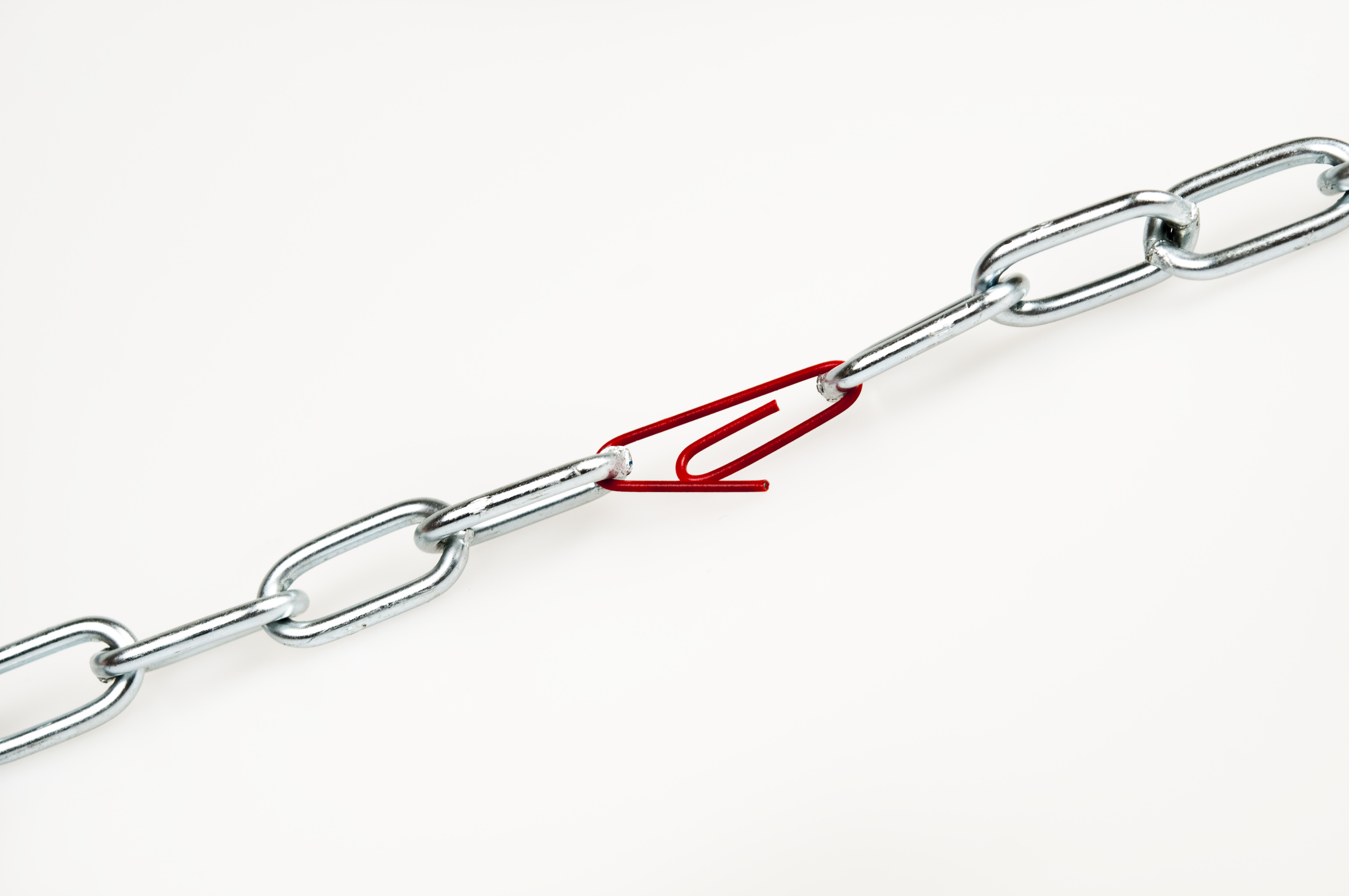 Chrome chains held together by a red paper clip signifying the weak link in a process.